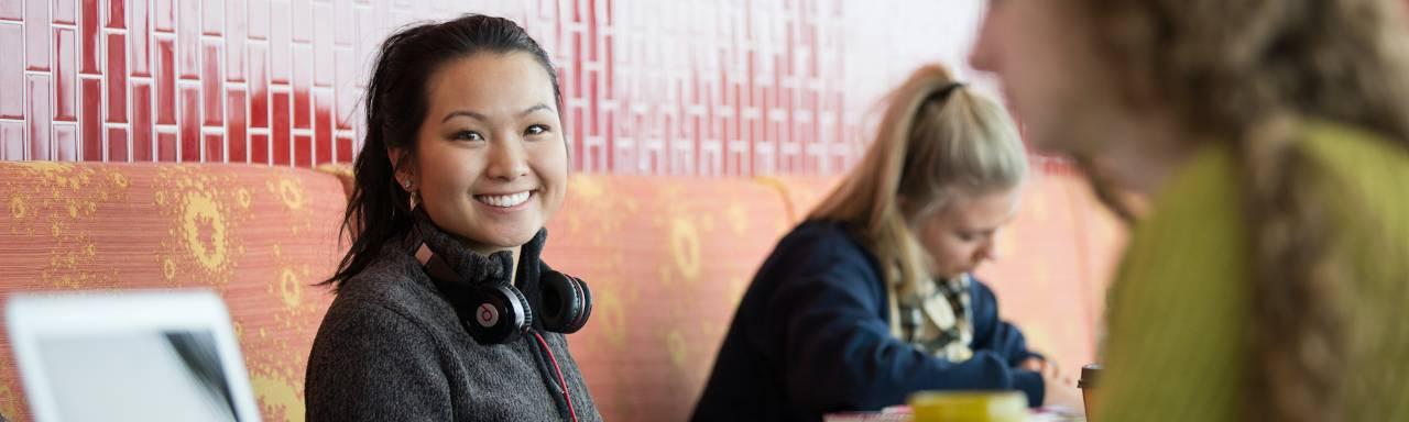 Photo of a female student smiling at the camera with headphones around her neck.